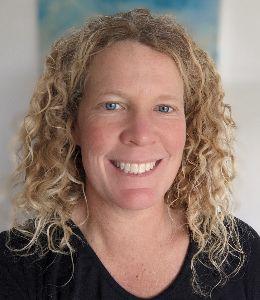 Dr. Seegers smiles into the camera, face framed by curly blonde hair. She is wearing a black shirt.