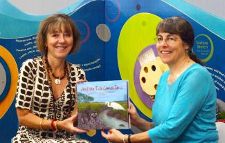 State Librarian Julie Walker, left, and University of Georgia marine sciences professor Merryl Alber hold up “And the Tide Comes In,” a children’s book on salt marshes now available at every public library in the state