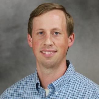 Dr. Greer smiles for a headshot in a blue plaid button up