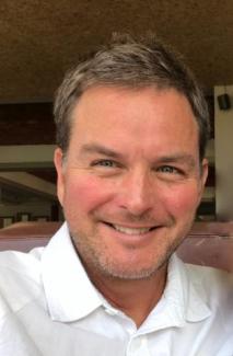 Dr. Lundemo smiles at the camera in a white button up and close cut salt and pepper hair.