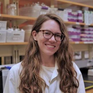 Dr. Johnson with long strawberry blonde hair and dark framed glasses, stands in a white lab coat smiling into the camera.