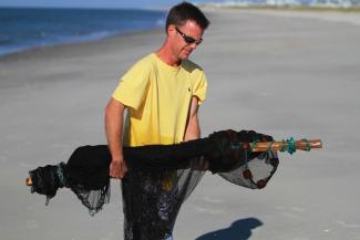 Dr. Hancock carries a black net across the beach in a yellow t-shirt and sunglasses