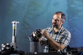 Dr. Brock Woodson sits in a green plaid shirt tinkering with a mechanical instrument