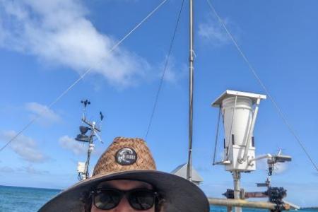 A bearded white man in a straw hat with ocean and rocks in the background.