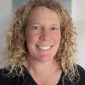 Dr. Seegers smiles into the camera, face framed by curly blonde hair. She is wearing a black shirt.