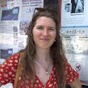 Dr. Brasseale smiles into the camera wearing a red floral dress with her sunglasses pushed back on her head. Her long hair is slightly windswept and she looks into the camera confidently