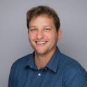 Dr. Cyronak smiles for a headshot in a blue button up