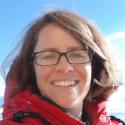 Dr. Nicole Millette smiles into the camera in a headshot photo, wearing a red coat and box frame glasses.