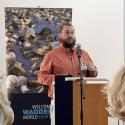 Dr. Philip Riekenberg lectures in a salmon button up in front of a poster of oysters. 