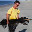 Dr. Hancock carries a black net across the beach in a yellow t-shirt and sunglasses