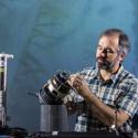 Dr. Brock Woodson sits in a green plaid shirt tinkering with a mechanical instrument